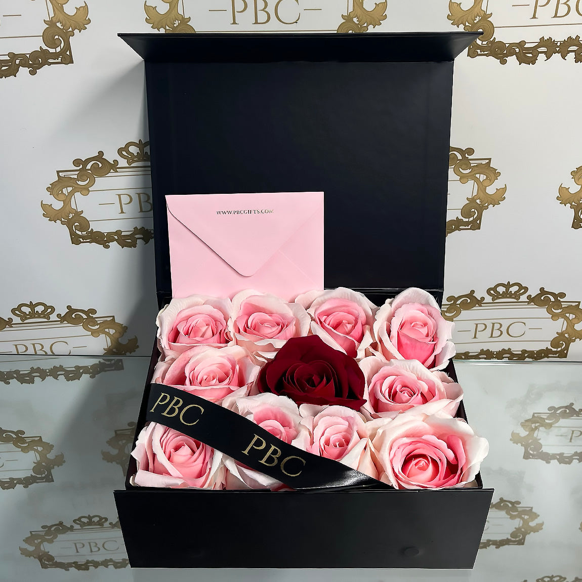 Black rectangle box with pink envelope, pink a roses and a single centre red rose